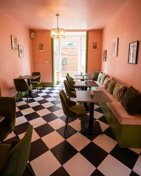 Peach dining room with black and white checkerboard floor and olive velvet chairs